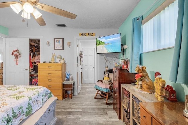 bedroom with ceiling fan, a spacious closet, a textured ceiling, light hardwood / wood-style floors, and a closet