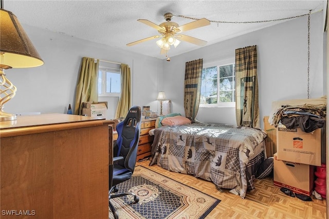 bedroom with ceiling fan, light parquet floors, and a textured ceiling