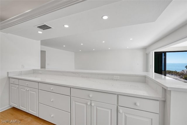 kitchen with white cabinets, light hardwood / wood-style floors, light stone counters, and kitchen peninsula