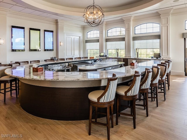 bar with an inviting chandelier, light hardwood / wood-style floors, a raised ceiling, and light stone counters