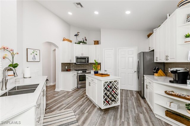 kitchen featuring white cabinets, sink, light hardwood / wood-style flooring, a towering ceiling, and appliances with stainless steel finishes