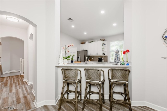 kitchen featuring white cabinetry, stainless steel fridge with ice dispenser, backsplash, light hardwood / wood-style floors, and a kitchen bar