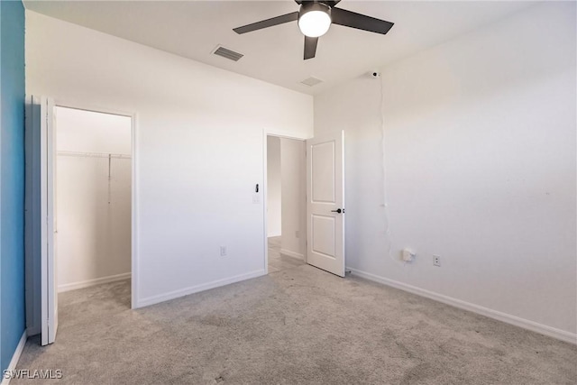 unfurnished bedroom with light carpet, a walk in closet, a closet, and ceiling fan