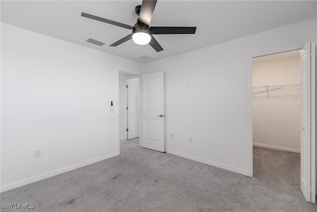 unfurnished bedroom featuring a closet, a walk in closet, light colored carpet, and ceiling fan