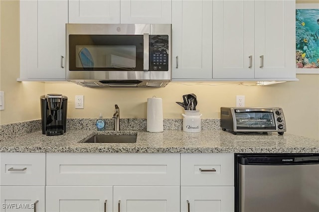 kitchen with light stone counters, refrigerator, sink, and white cabinets