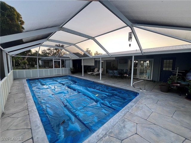 pool at dusk with glass enclosure and a patio area