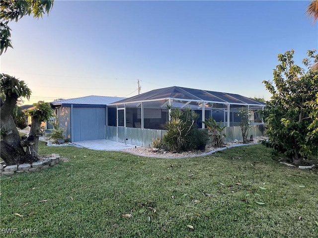 back house at dusk featuring glass enclosure and a lawn