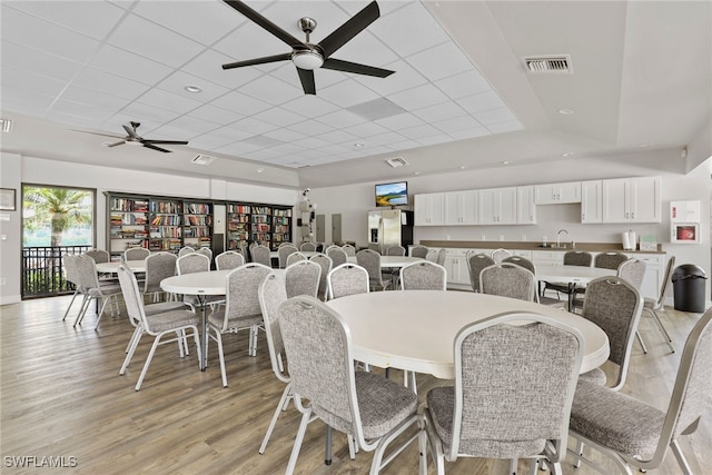 dining space featuring ceiling fan, a drop ceiling, light wood-type flooring, and sink