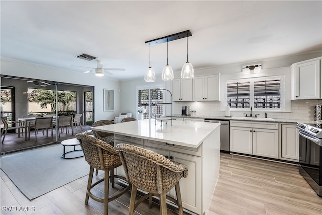 kitchen with appliances with stainless steel finishes, backsplash, a center island with sink, decorative light fixtures, and a breakfast bar area