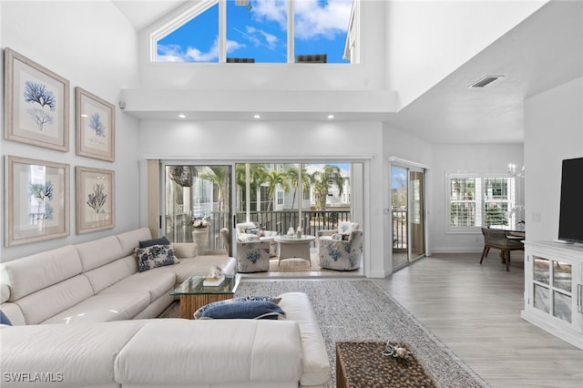 living room with a chandelier, a towering ceiling, a wealth of natural light, and light hardwood / wood-style floors