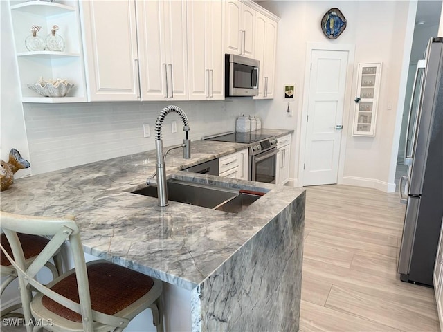 160 Barefoot Cir Unit 38, Bonita Springs, FL 34134 - kitchen with a peninsula, white cabinetry, light stone counters, a sink, and appliances with stainless steel finishes