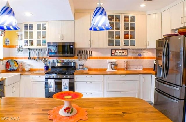 kitchen with decorative backsplash, white cabinetry, butcher block counters, and stainless steel appliances