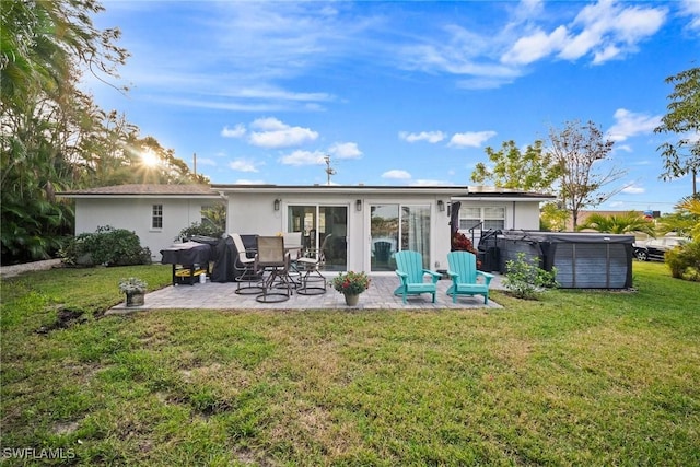 back of property with a yard, a patio, and a hot tub