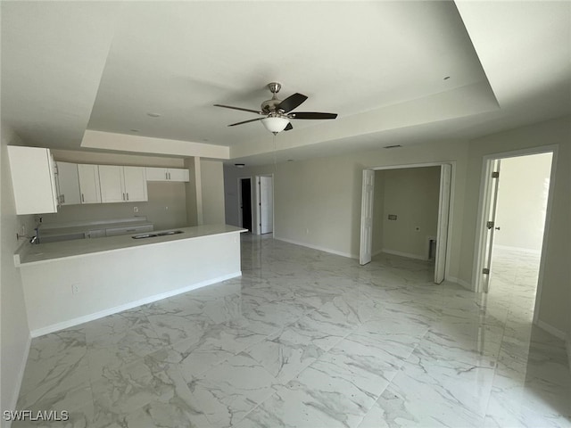 kitchen with white cabinets, sink, ceiling fan, a tray ceiling, and kitchen peninsula