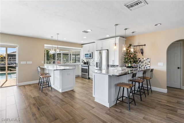 kitchen with pendant lighting, kitchen peninsula, a breakfast bar area, white cabinetry, and stainless steel appliances