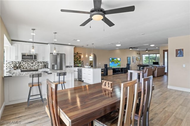 dining room with light wood-type flooring, wine cooler, and ceiling fan