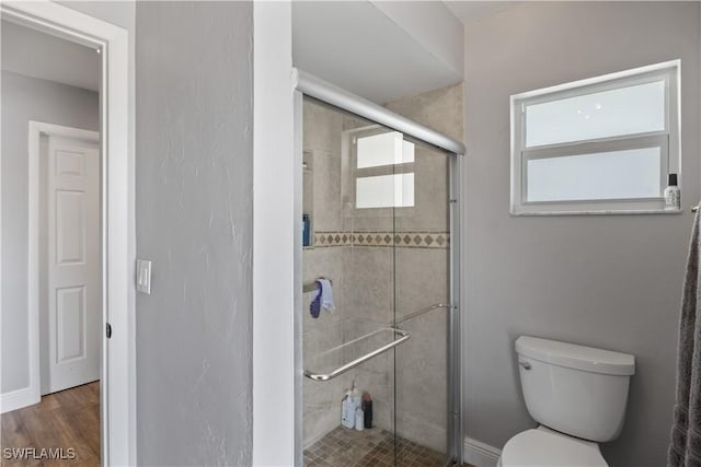 bathroom featuring a shower with door, plenty of natural light, wood-type flooring, and toilet