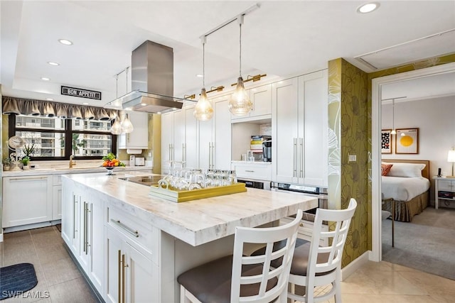 kitchen with white cabinets, a kitchen bar, island range hood, and light stone counters