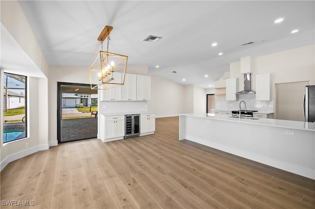 kitchen with lofted ceiling, wine cooler, pendant lighting, wall chimney exhaust hood, and white cabinets