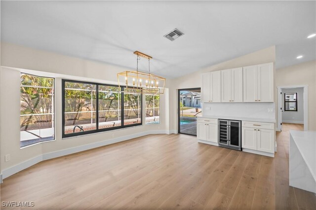 kitchen featuring wine cooler, vaulted ceiling, light hardwood / wood-style floors, pendant lighting, and white cabinets