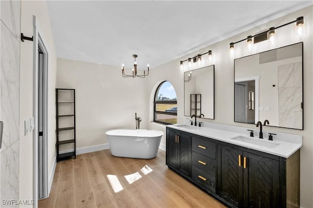 bathroom featuring an inviting chandelier, a tub to relax in, wood-type flooring, and vanity