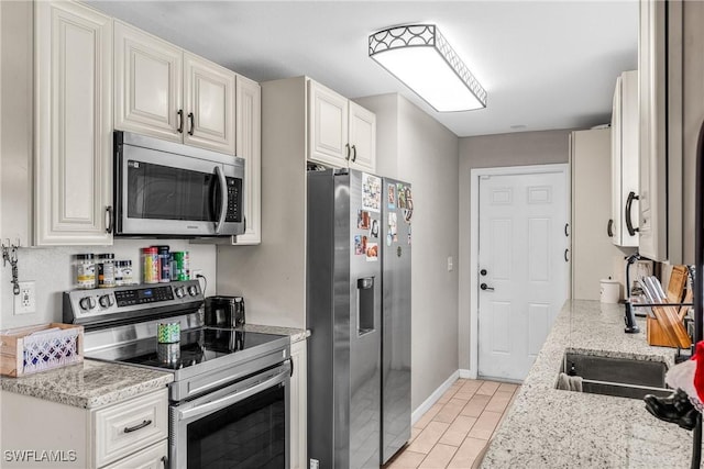 kitchen with appliances with stainless steel finishes, light tile patterned floors, white cabinetry, and light stone counters