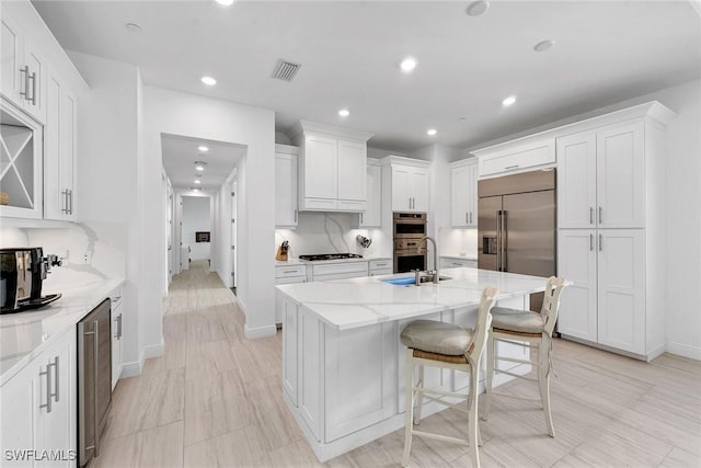 kitchen with light stone countertops, white cabinetry, and a kitchen island with sink