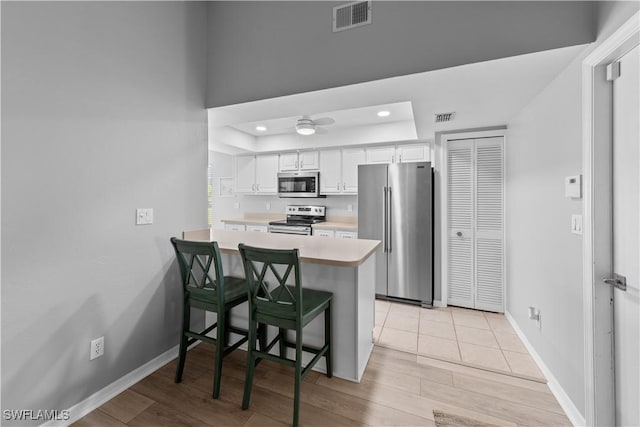 kitchen featuring a breakfast bar, a raised ceiling, white cabinets, kitchen peninsula, and stainless steel appliances