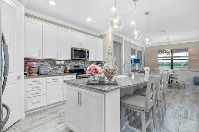 kitchen featuring white cabinets, appliances with stainless steel finishes, hanging light fixtures, and an island with sink