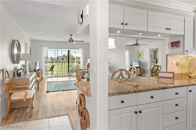 kitchen featuring backsplash, ceiling fan, light stone countertops, light hardwood / wood-style floors, and white cabinetry