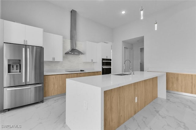 kitchen with pendant lighting, white cabinets, wall chimney range hood, an island with sink, and stainless steel fridge with ice dispenser