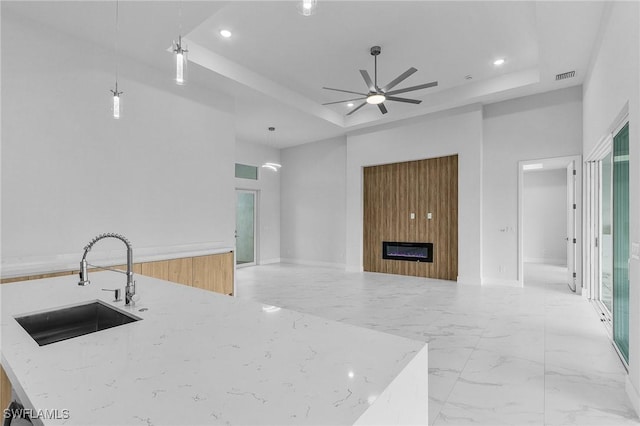 kitchen featuring decorative light fixtures, light stone counters, a raised ceiling, and sink