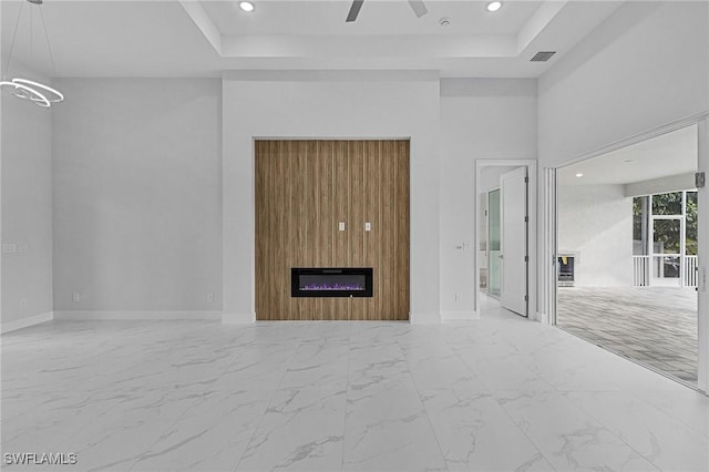 unfurnished living room with a raised ceiling, ceiling fan, and a large fireplace