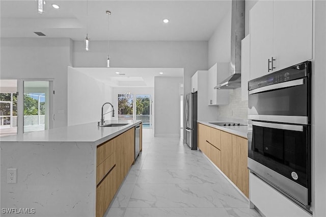 kitchen featuring a center island with sink, wall chimney range hood, sink, white cabinetry, and stainless steel appliances