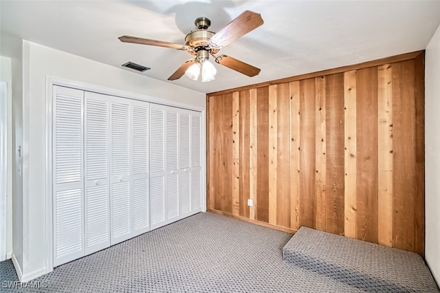 unfurnished bedroom featuring carpet floors, a closet, ceiling fan, and wooden walls