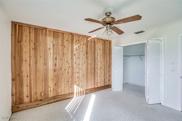 unfurnished bedroom with a closet, ceiling fan, and wood walls