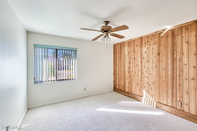 spare room with wood walls, carpet, and ceiling fan