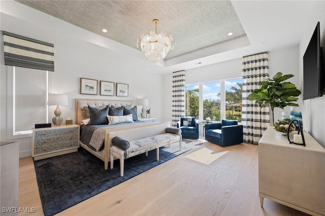 bedroom featuring a chandelier, light wood-type flooring, and a raised ceiling