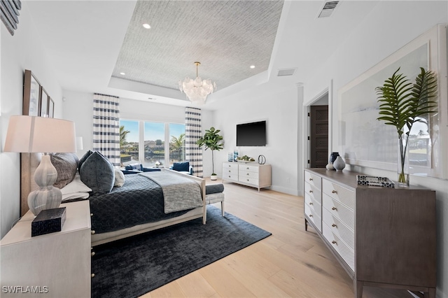 bedroom featuring a chandelier, light wood-type flooring, and a raised ceiling