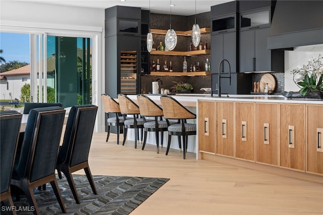 bar featuring ventilation hood, sink, hanging light fixtures, tasteful backsplash, and light hardwood / wood-style floors