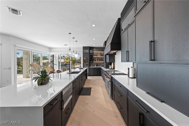 kitchen with a large island, hanging light fixtures, light hardwood / wood-style flooring, high end stainless steel range, and custom exhaust hood