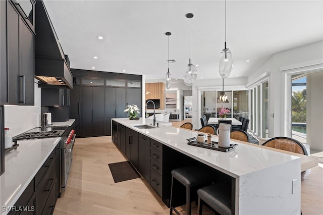 kitchen with a kitchen bar, light wood-type flooring, sink, a large island with sink, and hanging light fixtures