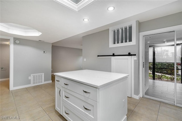 kitchen with a barn door, a center island, white cabinets, and light tile patterned floors