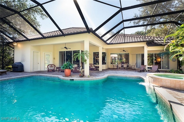 view of pool featuring glass enclosure, ceiling fan, an in ground hot tub, and a patio