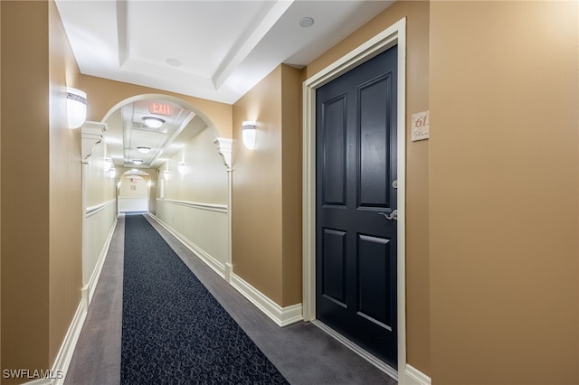 hallway featuring dark carpet and a tray ceiling