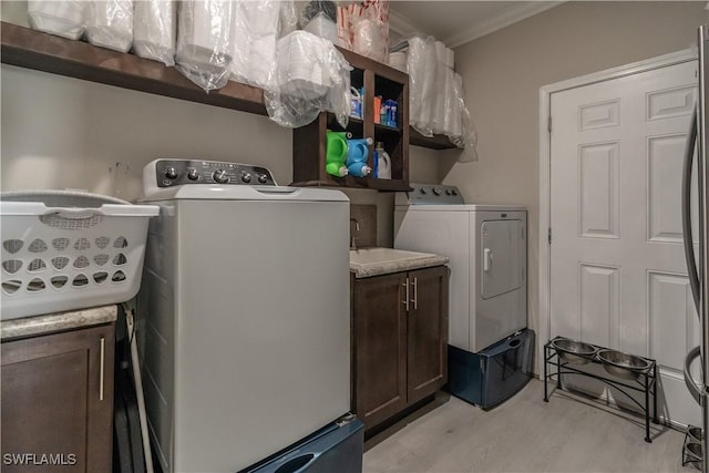 washroom featuring cabinets, ornamental molding, sink, washer and dryer, and light hardwood / wood-style flooring