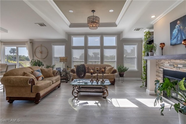 living room with hardwood / wood-style floors, a stone fireplace, a raised ceiling, and crown molding