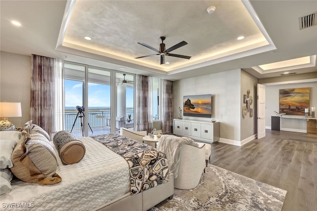 bedroom featuring a tray ceiling, ceiling fan, wood-type flooring, and access to outside