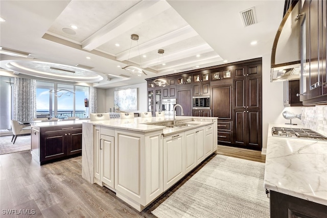 kitchen with built in microwave, sink, stainless steel gas cooktop, light hardwood / wood-style flooring, and a large island with sink