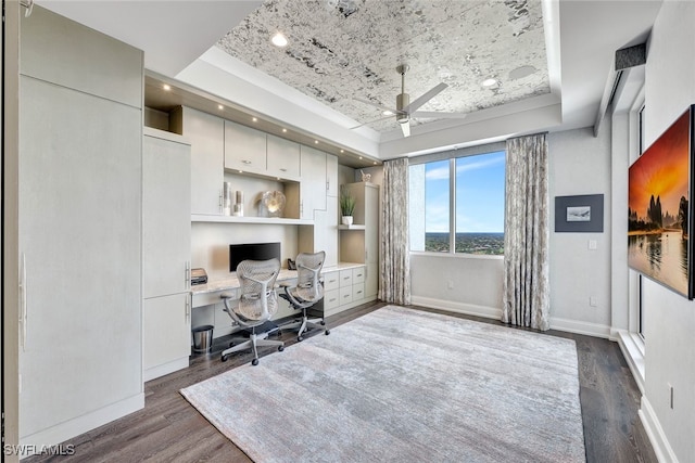 office with dark hardwood / wood-style flooring, ceiling fan, a raised ceiling, and built in desk